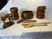 Wooden mushrooms salt and pepper shakers, bowls and wooden serving utensils laid flat on white fabric