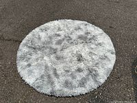 Round light grey shag rug placed on pavement, showing full circular shape and plush texture.