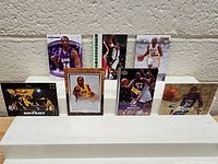 Seven Kobe Bryant basketball cards displayed on a white stand against a beige wall showing various action and portrait shots.