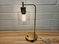 Front angle photo of brass desktop lamp with clear glass shade showing Edison-style bulb, dimmer knob on base, and power cord.