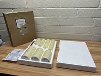 Photo showing six ivory flameless LED candles in styrofoam packaging, cardboard box in background, and user manual on table.