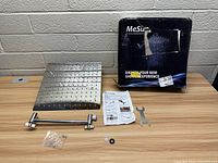 Large square stainless steel rainfall shower head next to its mounting arm, screws, small wrench, rubber washer, instruction manual, and branded box.