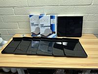 Photo showing two unopened 4-pack boxes of Boxy Concepts Hat Organizer shelves with 6 individual black shelves laid out on a wooden surface against a white brick wall.