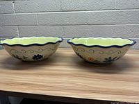 Front view of two Pfaltzgraff hand painted bowls showing yellow interior and floral exterior design with scalloped dark blue rim.