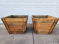 Front view of two square wooden planter boxes showing wood slats and metal reinforcements.