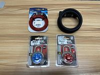 Four combination locks arranged on wood surface: two Master dial padlocks in packaging, one red WordLock cable lock still in packaging, one black coiled cable lock unboxed.