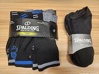 Pack of six Spalding crew socks in black, grey, and blue, showing the packaging and branding