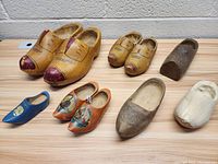 Seven pairs and singles of vintage wooden shoes and clogs arranged on a surface, showing carved details and painted decorations.