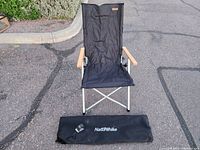 Front view of new black Naturehike folding chair with wooden armrests and aluminum frame alongside the black carry bag.