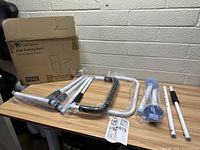 Oasis Space bed safety rail components laid out on table with assembled frame parts wrapped in plastic, including white metal bars and black connectors.