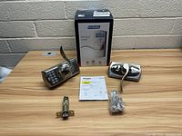 Photo showing electronic keypad lever lock with keypad on front, matching interior lever, latchbolt, keys, and instruction manual on wood surface with box in background.