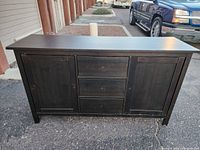 Frontal view of the wooden TV stand/credenza showing two cabinet doors and three central drawers without knobs.