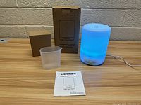 New URPower essential oil diffuser glowing blue, with the original packaging box, measuring cup, and instruction manual.
