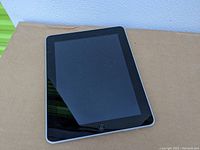 Front view of the Apple iPad tablet showing black screen and home button, device is powered off or in sleep mode.
