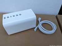 Side view of white Apple Airport router and coiled white power cable on cardboard surface