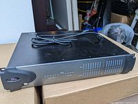 Front-left angled view of the Avid HD I/O interface showing power cord on top and the front panel with Avid logo and power button.
