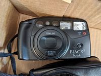 Front view of Blacks Insight point and shoot camera inside box, showing lens and flash