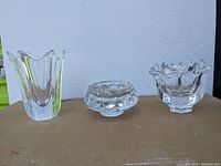 Three signed Orrefors crystal items: two vases and a bowl arranged side by side on a flat surface with light background