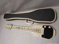 Lap steel guitar laid next to open fitted hard case showing front and case exterior