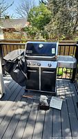 Full front view of grill on deck showing lid, control panel, side burner and cover draped
