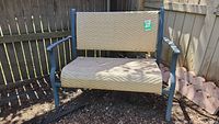 Front view of metal two person outdoor bench with woven light tan seat and backrest.