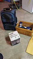 Photo of the Coleman propane lantern box, black and gray backpack, and wicker basket with two battery lanterns and umbrella inside