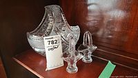 Three decorative baskets on a wooden shelf showing clear glass and crystal with handles