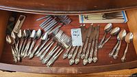 Full set of Laguiole de Table stainless steel cutlery laid out in drawer showing 49 pieces including serving spoons, dinner forks, dinner spoons, dessert forks, and knives.