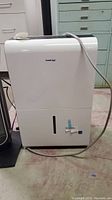 Front view of white KoolKing dehumidifier with water tank window and power cord draped