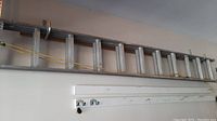 Full view of the aluminum extension ladder hung horizontally, showing yellow extension rope and weathered condition.