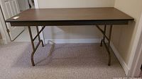 Full view of the portable folding table showing the wood grain laminate surface and metal folding legs.