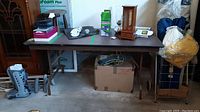 Full view of folding table with wood top placed in garage among various other items.