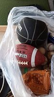 Photo showing two basketballs, a Wilson football, and worn baseball gloves inside plastic bag.