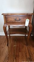 Front view of the wooden side table showing the one drawer with decorative handle and curved legs.