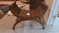 Full view of the Roman-style vintage wood bench showing the curved slatted seat and arched legs on a carpeted floor.