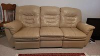 Front view of a beige leather three-seater sofa with cushioned backrests and recliner sections at each end.