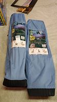 Two blue carrying bags for twin size BYO bed frames by Woods laid on concrete floor with instruction labels visible.