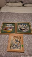 Overview of the three framed needlepoint pictures spread on a bed with paisley fabric background