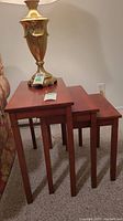 Three wooden nesting tables stacked together, reddish-brown finish.