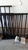 Black metal railing sections leaning against wall with a white basket on the floor in front containing hardware pieces