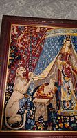 Close-up of the left side of the needlepoint showing the lion and stitching detail with the wooden carved frame and gold trim.