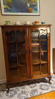 Front view of vintage wooden cabinet with glass panel doors, showing overall structure and visible cracks and detachments.