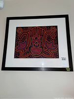 Frontal view of framed textile wall art showing symmetrical bright leaf and flower design in black frame.
