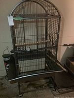 Front view of large bird cage on metal stand with wheels, showing curved top and bars