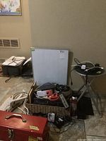 Photo showing whiteboard standing against the wall, various power cords and tools in a wicker basket, cordless phones on a small foldable stool.