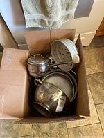 Box containing assorted pots, pans, colander, and steamer insert