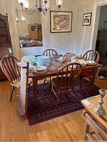 The wood dining table with chairs around, top view scattered with dishes (not included), hardwood floor and a decorative rug underneath.