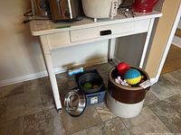 White wooden table with metal top and single drawer from front angle, showing drawer handle and wear on legs. Floor tile visible.