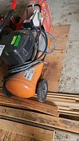 Side view showing the orange tank and attached hose and motor housing of the electric air compressor