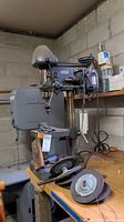 Full view of Atlas drill press sitting on a workbench with extra grinding wheels and belts placed in front.